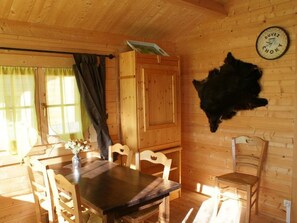 A wooden cabin interior with a dining table, chairs, a clock, and a fur piece on the wall.