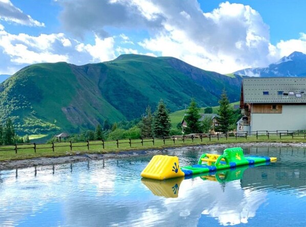 A mountain landscape with a body of water, a wooden house, and a fenced area with colorful floating objects.
