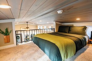 Une chambre avec un plafond en bois, un lit avec une literie verte, une vue sur l’extérieur et une petite table avec une lampe.