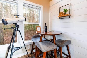 Une pièce comprenant un télescope, une table ronde, deux chaises, un tableau encadré, une bouteille et une plante posée sur une étagère.