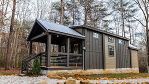 A modern cabin with a covered porch, large windows, and a stone foundation.