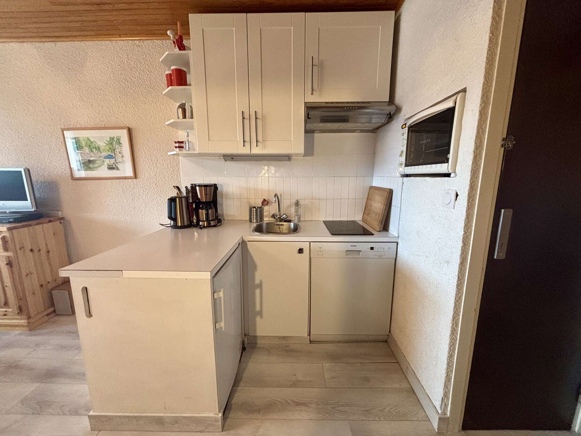 A compact kitchen with a dishwasher, a sink, and a stove. There is a small countertop with a coffee maker and a picture frame on the wall.