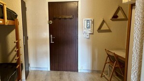 Una habitación con puerta de madera, una mesita pequeña, un enchufe en la pared y un estante triangular.
