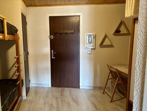 Ein Zimmer mit Holztür, einem kleinen Tisch, einer Wandsteckdose und einem dreieckigen Regal.
