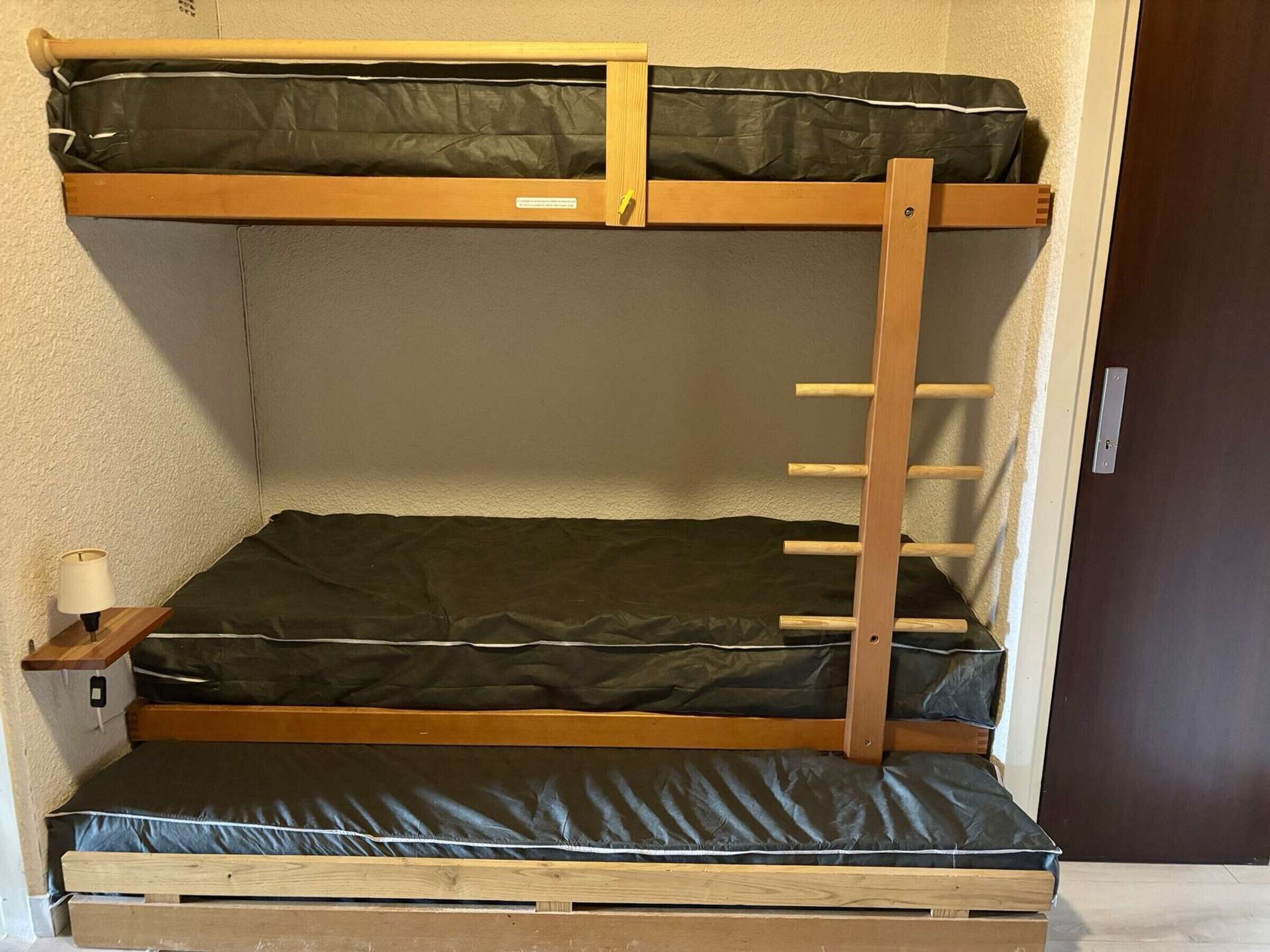 A bunk bed with a wooden frame, two mattresses, and a pull-out desk with a lamp.
