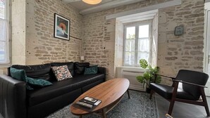 Een kamer met een stenen muur, een zwarte leren bank, een houten bijzettafeltje, een zwarte fauteuil en een raam met uitzicht.