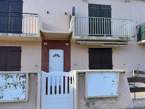 A multi-story building with numbered doors, a white entrance gate, and balconies with metal railings. - Seaside apartment - 4 guests (Fleury-Saint-Pierre-la-Mer)