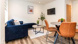 Een moderne woonkamer met een donkerblauwe bank, een ronde tafel en oranje stoelen.