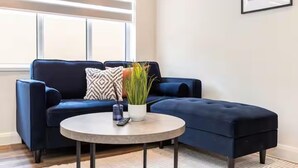 Een moderne woonkamer met een donkerblauwe modulaire bank, een ronde salontafel en een potplant.