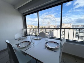 Mesa de jantar posta com pratos, copos e talheres, com vista para a paisagem urbana e uma roda gigante.