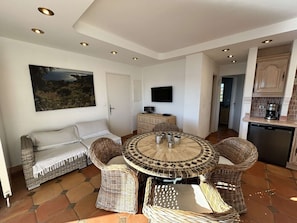 A dining area with wicker furniture, a tiled floor, a television, and a kitchen with a coffee machine. - 3-Room Apartment in Port Grimaud II with Sea View and Wi-Fi (Port Grimaud)