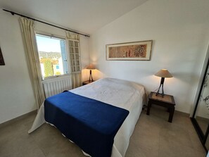 A bedroom with a bed, two bedside lamps, a window with curtains, and a painting on the wall. - 3-Room Apartment in Port Grimaud II with Sea View and Wi-Fi (Port Grimaud)