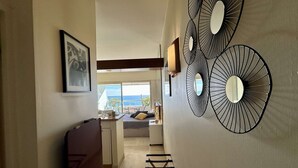 A hallway with a bed, a desk, and a chair. There are three wall-mounted mirrors and a framed picture on the wall. - Stunning studio with sea view - 2 guests (Villeneuve-Loubet)