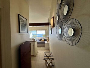 A hallway with a bed, a desk, and a chair. There are three wall-mounted mirrors and a framed picture on the wall. - Stunning studio with sea view - 2 guests (Villeneuve-Loubet)