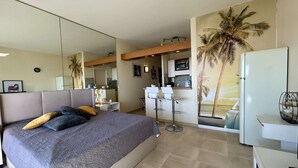 A modern bedroom with a large bed, a desk, and a kitchenette. - Stunning studio with sea view - 2 guests (Villeneuve-Loubet)