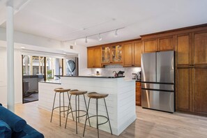 Una cocina moderna con armarios de madera, un refrigerador de acero inoxidable y una zona con taburetes de bar.