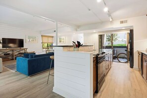A modern living room with a blue sofa, a flat-screen TV, and a kitchen area with a stove and cabinets. - 2BR Hilton Head Villa | 3 Pools + Bike to Coligny in 5 Min (Hilton Head Island)