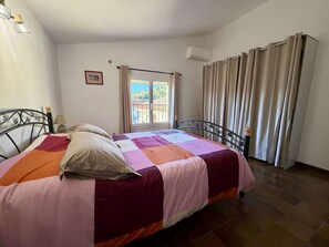 A bedroom with a bed, a window with curtains, a wall-mounted air conditioner, and a small bedside table with a lamp. - Charming duplex near the sea, 4 guests (Borgo)