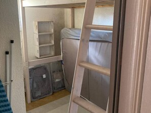 Une petite pièce comprenant un lit superposé, une échelle et des bacs de rangement.