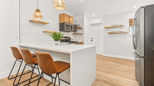 A modern kitchen with a central island, wooden bar stools, pendant lights, and built-in appliances. - The Golden Hour Mirage|Hot Tub|Game Room|Near Park (Joshua Tree)