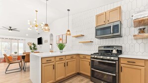 A modern kitchen with a central island, wooden cabinets, a stainless steel stove, and a microwave. - The Golden Hour Mirage|Hot Tub|Game Room|Near Park (Joshua Tree)
