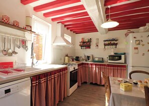 Una cocina con cortinas a cuadros rojos y blancos, un lavavajillas Bosch, un microondas y un refrigerador con imanes.