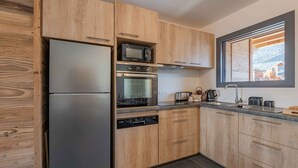 Uma cozinha moderna com armários de madeira, uma geladeira de aço inoxidável, micro-ondas, forno e janela com vista para edifícios.