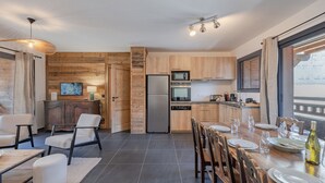 Uma cozinha moderna com armários de madeira, uma geladeira e um espaço de refeições com uma mesa posta para quatro pessoas.