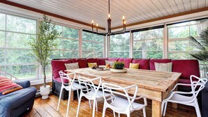 Ein Holztisch, umgeben von weißen Stühlen, einer rot gepolsterten Bank und einem Blumentopf.