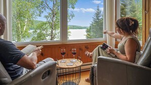 Ein Zimmer mit einem großen Fenster, einem runden Holztisch mit zwei Gläsern Rotwein und zwei Ledersesseln.