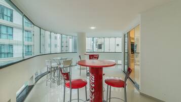 Um interior moderno com uma mesa redonda e cadeiras vermelhas, grandes janelas e uma mesa com a marca Coca-Cola.