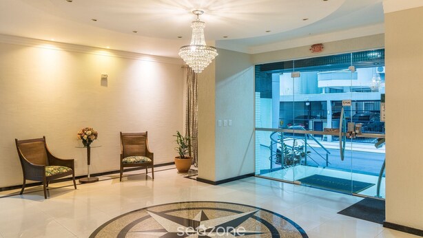 A lobby with two wooden chairs, a chandelier, a potted plant, and a glass door leading to a lower level.