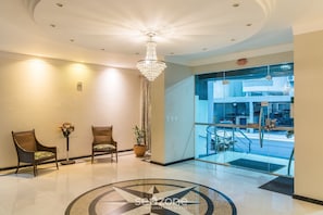 A lobby with two wooden chairs, a chandelier, a potted plant, and a glass door leading to a lower level. - Apt w/ BBQ 350m From the Beach Apv0202 (Itapema)