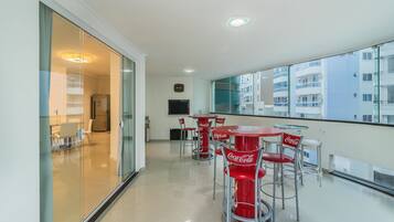 Um apartamento moderno com varanda, mobiliado com cadeiras e mesas com a marca Coca-Cola em vermelho, e vista para a cidade.
