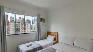 A hotel room with a bed, a window with curtains, and a view of city buildings.