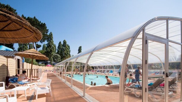 Een overdekt zwembadgedeelte met ligbedden en parasols.