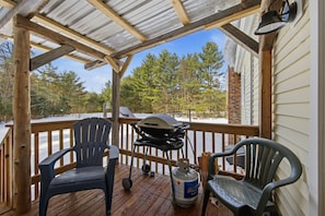 A covered outdoor deck with two Adirondack chairs, a grill, and a propane tank.