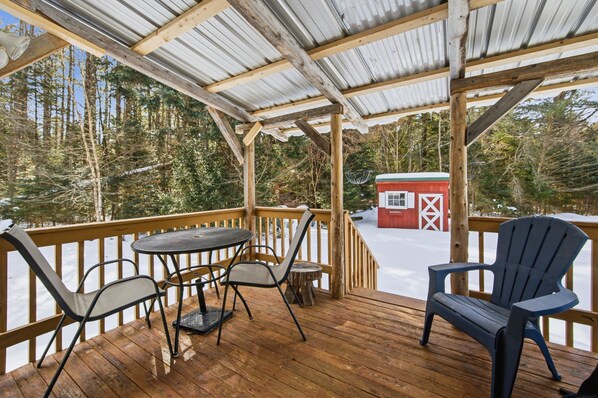 Una terraza de madera con una mesa y sillas, con vistas a un paisaje nevado y un edificio rojo.