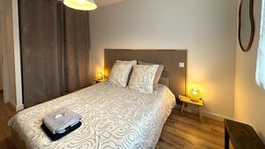 A bedroom with a large bed, two bedside lamps, a hanging light, and a wooden nightstand.
