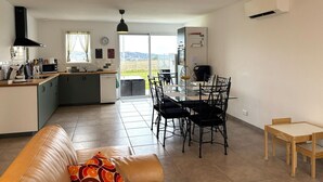 A modern kitchen with a dining area, a sofa, and a view of the countryside.