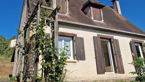Ein zweigeschossiges Haus mit geneigtem Dach, Holzläden und einem Schornstein.