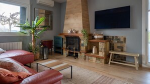 Ein Wohnzimmer mit Kamin, Deckenventilator, großem Fenster und Wand-Fernseher.