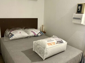 Ein Bett mit einer grauen Bettdecke und zwei Kissen, eines davon mit dem Aufdruck "Anti-acariens".