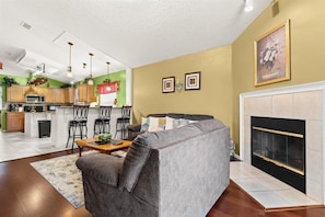 A modern living room with a grey sofa, a fireplace, and a kitchen in the background.
