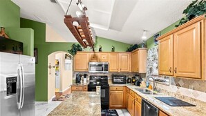 A modern kitchen with wooden cabinets, stainless steel appliances, and a granite countertop. - The River City Retreat (Jacksonville)