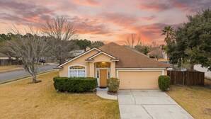 A single-story house with a front garage, a driveway, and a well-maintained lawn. - The River City Retreat (Jacksonville)