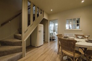 A staircase leading to a second floor, a dining area with a table set for four, and a refrigerator in the kitchen area.