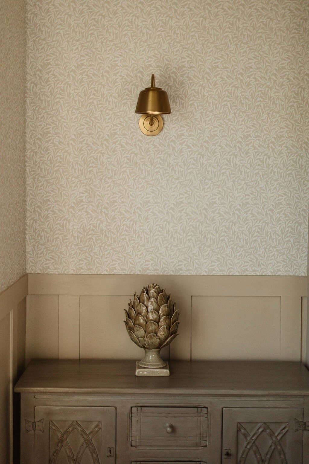 En væg med et struktureret mønster, en vægmonteret lampe og en dekorativ genstand på et træskab.