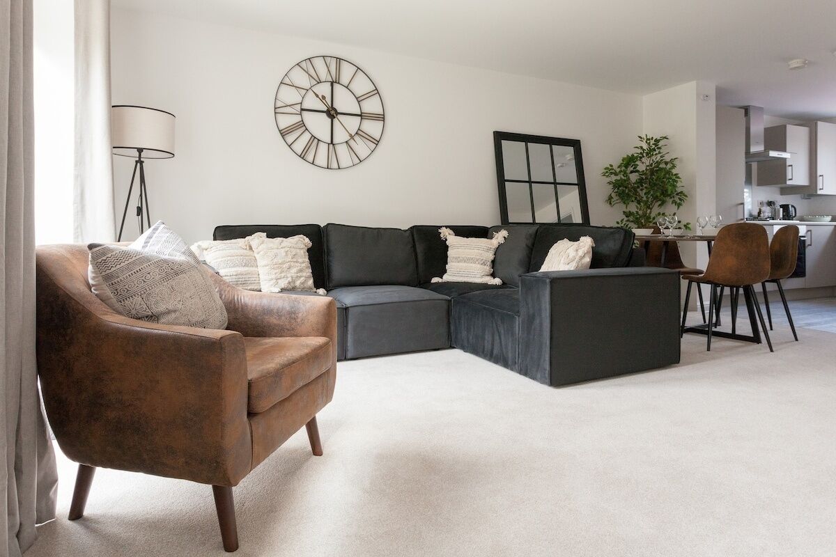 Una sala de estar moderna con un sofá modular, un sillón marrón y un comedor con mesa y sillas.