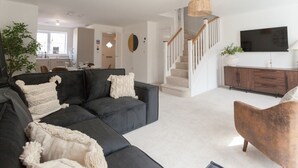 En moderne stue med en modulsofa, en brun lænestol og en trappe, der fører til en etage ovenover.